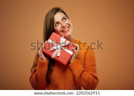 Happy dreaming woman in orange sweater holding gift box and looking up. Isolated female portrait in christmas style..