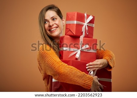 Happy woman in winter orange sweater holding stack of red gift boxes. Isolated female portrait in christmas style..