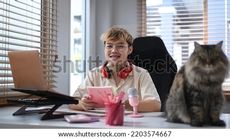 Young man sitting front of microphone and laptop at home studio with his lovely cat. Mass media, technology and people concept
