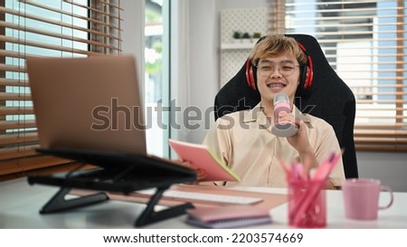 Asian male using microphone and laptop computer streaming audio podcast in home studio
