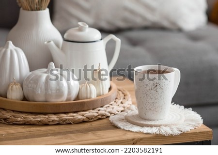 Still-life. Dried pampas grass in a vase, white ceramic pumpkins, a teapot, a cup and pumpkin-shaped candles on a coffee table in the home interior of the living room. Cozy autumn concept.