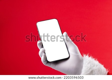 Image of hand of santa claus holding smartphone with blank screen and copy space on red background. Christmas, connection, technology, tradition and celebration concept. Royalty-Free Stock Photo #2203596503