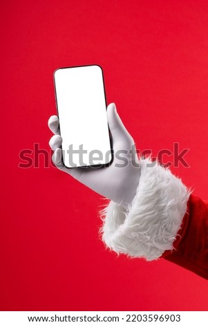 Image of hand of santa claus holding smartphone with blank screen and copy space on red background. Christmas, connection, technology, tradition and celebration concept. Royalty-Free Stock Photo #2203596903