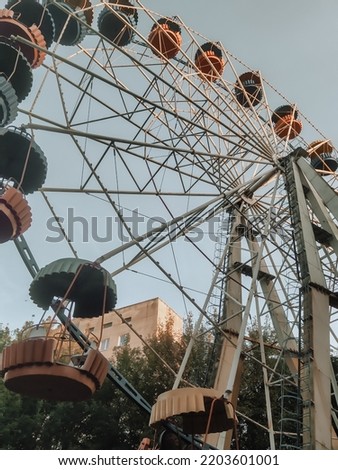 A ferris wheel on the blue sky background. Old amusement park. Empty carousel in retro style. 20th century construction in Eastern Europe. Picture in soft muted color palette.