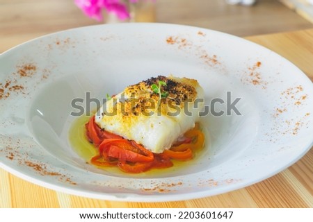 Delicious baked cod with roasted red pepper on wooden table.