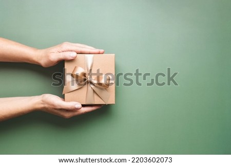 Female hands holding Christmas gift box on pastel green background. Royalty-Free Stock Photo #2203602073
