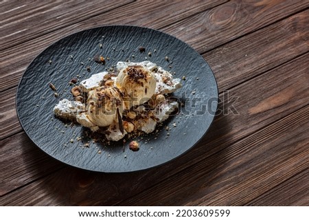 Ice cream balls with chocolate chips, hazelnuts, peanuts and meringues in a plate on a wooden table