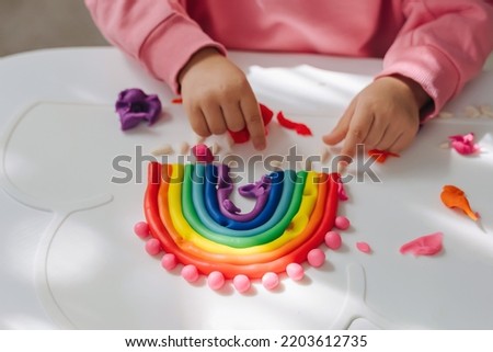 Child hands creating rainbow from play dough for modeling. Art Activity for Kids. Fine motor skills. Sensory play for toddlers. Royalty-Free Stock Photo #2203612735