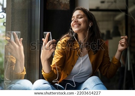 Young woman sitting and listening the music. Portrait of happy woman listening music with earphones while singing song.	