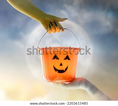 Halloween pumpkin basket in the hands of zombies and mummies on moon sky background.