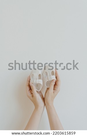 White cotton cute baby shoes in women's hands on white background. Fashion gender neutral baby clothes Royalty-Free Stock Photo #2203615859