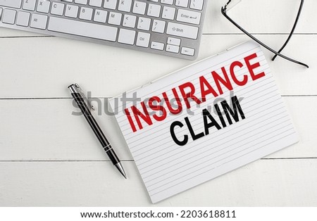 INSURANCE CLAIM text on notebook with keyboard , pen glasses on a white wooden background