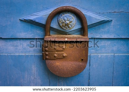 Close-up photograph of a blue-painted wooden door with an antique rusted metal padlock.