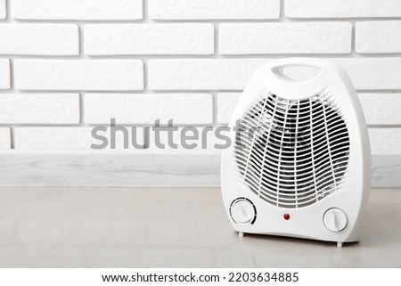 Electric fan heater near white brick wall