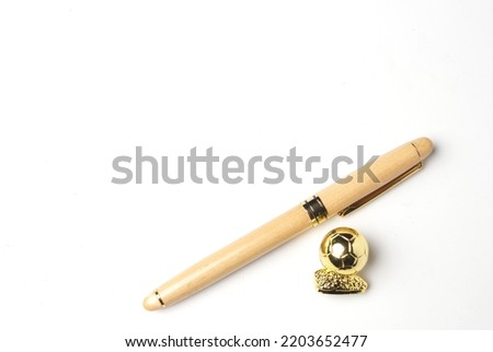 A picture of wooden pen with golden ball on copyspace white background. Signing good player in transfer window concept.
