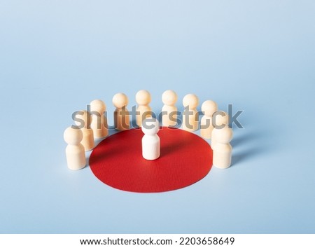 Wooden figures of people stand in a red circle, in the center of which is one white figure. The concept of a group, a society, a meeting. Royalty-Free Stock Photo #2203658649