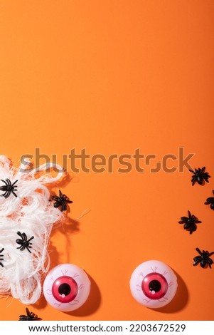 Multiple spider toys forming a spider web and scary eyes toys with copy space on orange background. halloween festivity and celebration concept