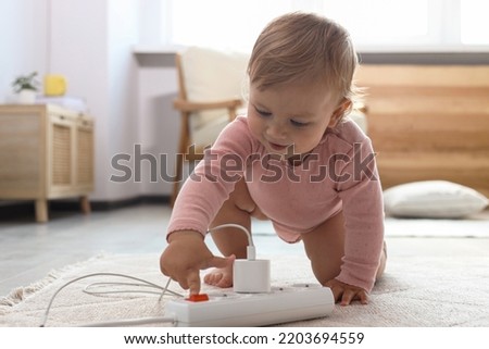 Cute baby playing with power strip on floor at home. Dangerous situation Royalty-Free Stock Photo #2203694559