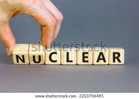 Nuclear or clear symbol. Businessman turns a cube and changes the word 'nuclear' to 'clear'. Beautiful grey background. Nuclear or clear and business concept. Copy space.