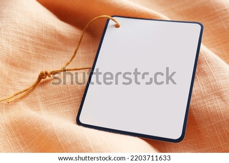 Cardboard tag with space for text on pale orange fabric, closeup