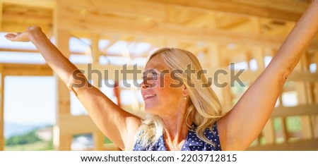 Excited senior woman inside of her new unfinished ecological wooden house.
