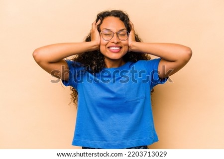 Young hispanic woman isolated on beige background laughs joyfully keeping hands on head. Happiness concept.