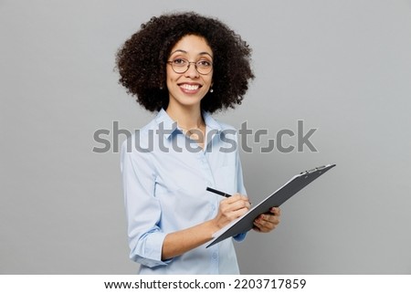 Young smiling fun employee business corporate lawyer woman of African American ethnicity in classic formal shirt work in office clipboard with papers document isolated on grey color background studio Royalty-Free Stock Photo #2203717859