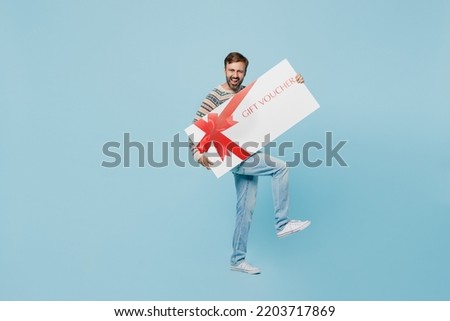 Full body young excited man 30s he wear sweater hold big gift certificate coupon voucher card for store isolated on plain pastel light blue cyan background studio portrait. People lifestyle concept