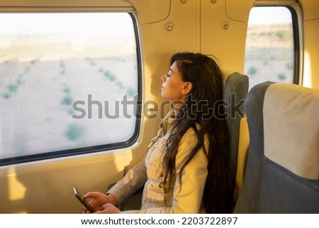 Pretty young female traveler traveling with classic train sitting near the window watching the scenery with her smartphone in hand. Concept travel, transport, smartphone.