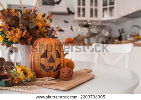 A vase of flowers,a jack pumpkin and candles on a tray. In the background - the interior of a white kitchen in Scandi style. The concept of home and comfort. Autumn decor for the Halloween holiday.