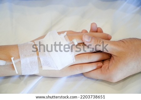 hand holding the hand of a sick kid and mother on bed were connected to the saline solution in hospital.