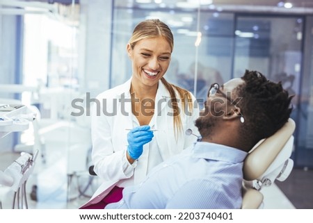 Young man patient having dental treatment at dentist's office. Female dentist working on patient's teeth. Man having teeth examined at dentists. Overview of dental caries prevention