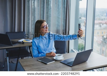 Smart female employee with netbook looking at camera during mobile call, successful freelancer in jacket talking on phone via app