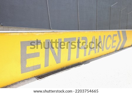 Closeup of arrow sign and inscription entrance on wall. Painted black and yellow on cement concrete wall on ramp of parking building