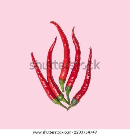 Flame made of red chili peppers on pastel light pink background. Minimalistic food composition. Creative spicy concept.