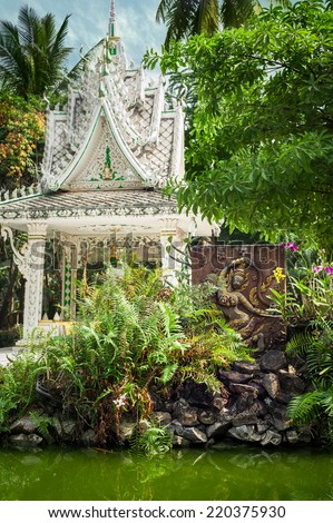 Buddhist carving and pagoda at outdoor park with decorative plants reflecting in pond. Asian city religious architecture at public place. Vientiane, Laos