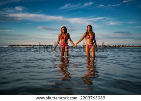 Young woman friends portrait walking together holding hands at the beach. Lifestyle concept.