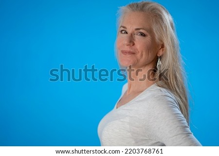 Turned to the side portrait of smiling happy, laughing mature woman isolated on solid blue background.