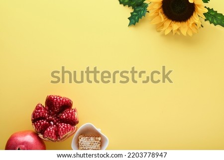 Rosh Hashanah. Ripe pomegranate, apple, honey and sunflower, yellow flowers on yellow background. composition with symbols jewish Rosh Hashanah holiday attributes. Top view with copy space.