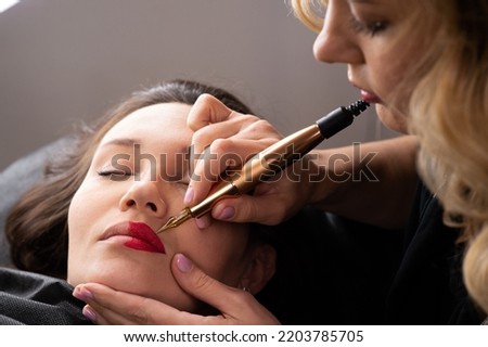 Young woman making lips tatouage in a dressing makeup room. Lips tatouage process .Woman making lips blushing. Make-up artist in beauty studio doing makeup for beautiful girl. Making mua. Royalty-Free Stock Photo #2203785705