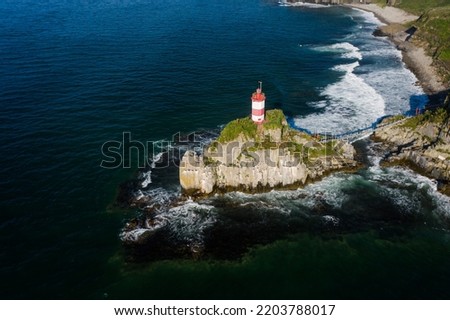 Basargin's lighthouse on a rocky island, to which the suspension bridge is stretched. The coastal beach. Vacation on the beach. Sea navigation. Drone view