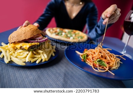 selective focus of burger with french fries and spaghetti near pizza and cropped woman on blurred background isolated on red