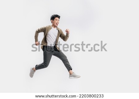 Full length Asian man running jumping in air gesture with happy smile on isolated white background. Cool man joyful running in copy space. Studio short. Royalty-Free Stock Photo #2203800233