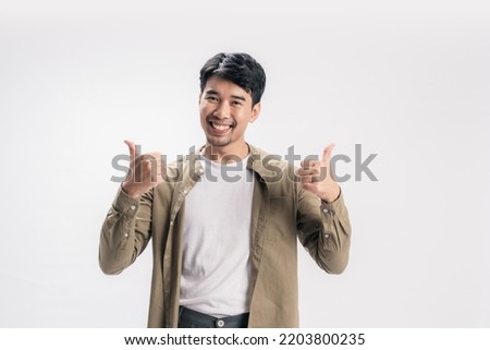 Portrait handsome asian man happy in a casual outfit, with his both hands showing thumbs up along with a cheerful smile on his face, giving the positive energy on isolated white background.