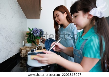 Asian cute mom teach daughter cooking food in kitchen at home for family day. Funny and smiling together. Smell and test good.