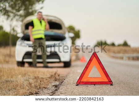 emergency triangles signaling a car breakdown and a man calling car insurance for assistance