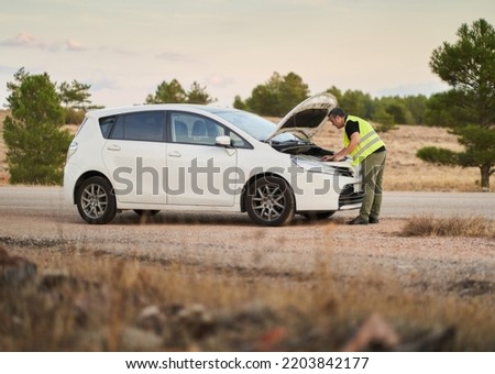 a man looking at his car's hot engine when he had a breakdown while traveling