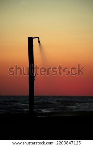 
silhouette of an open shower to the sea at sunset