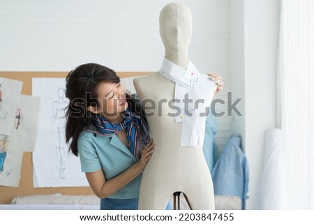 Young woman dressmaker using sketch paper measure measuring size of dress on the dummy mannequin in tailor shop. Fashion, dressmaking concept