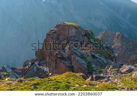 Awesome mountain landscape with cliff above abyss. Beautiful scenery with green grass near sharp rock near precipice edge. Scenic sunny view to green cliff with sharp stones at very high altitude. Royalty-Free Stock Photo #2203860037
